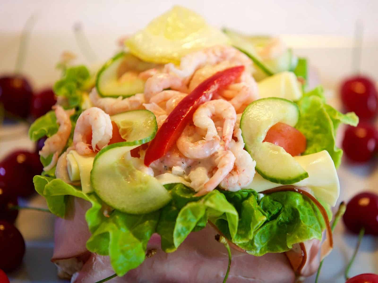 Närbild på en välfylld aptitlig räkmacka med oskarp bakgrund av körsbär